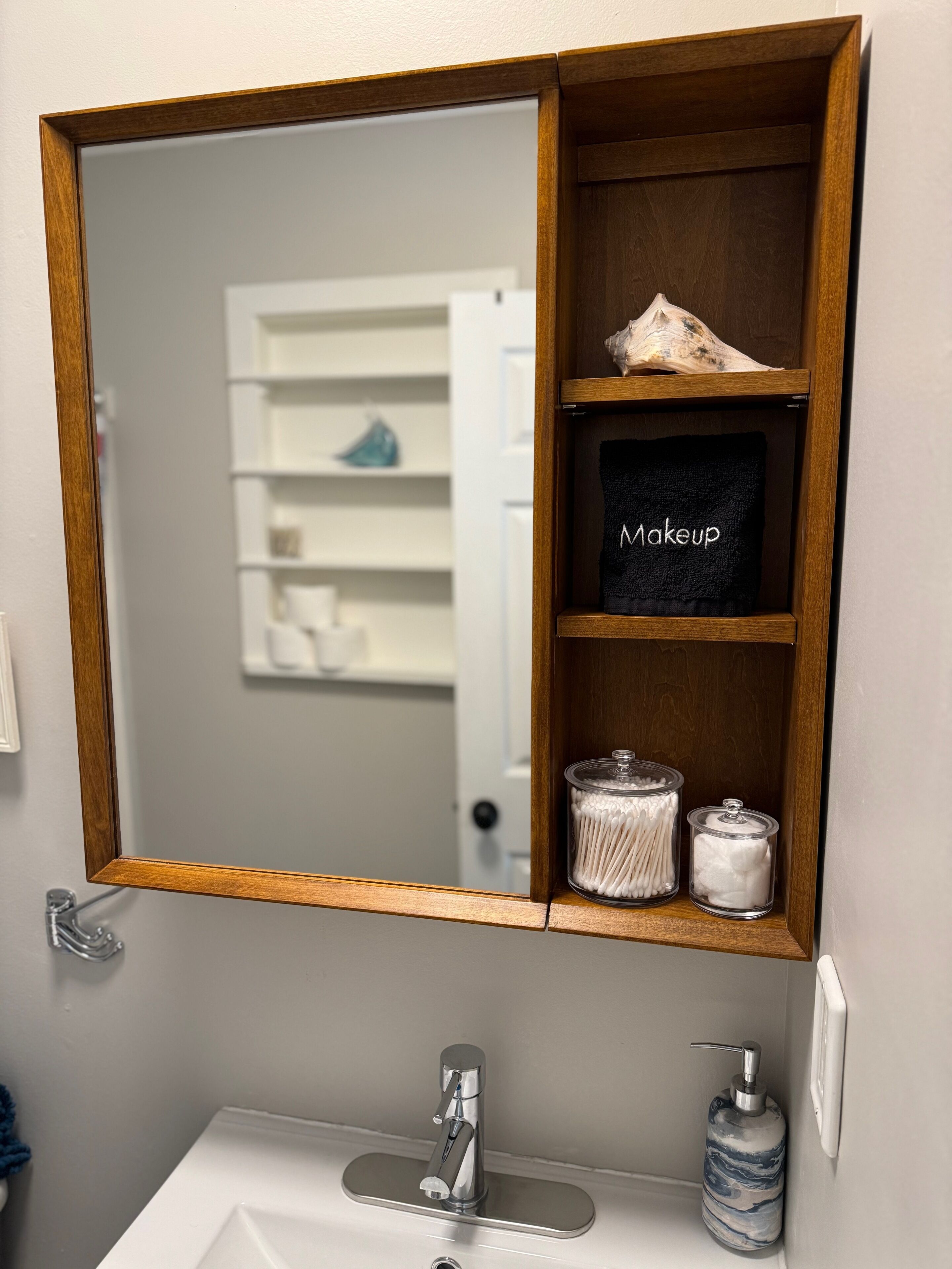 A bathroom with a wooden vanity, a mirror, a sink, and a shelf with a makeup towel and cotton swabs.