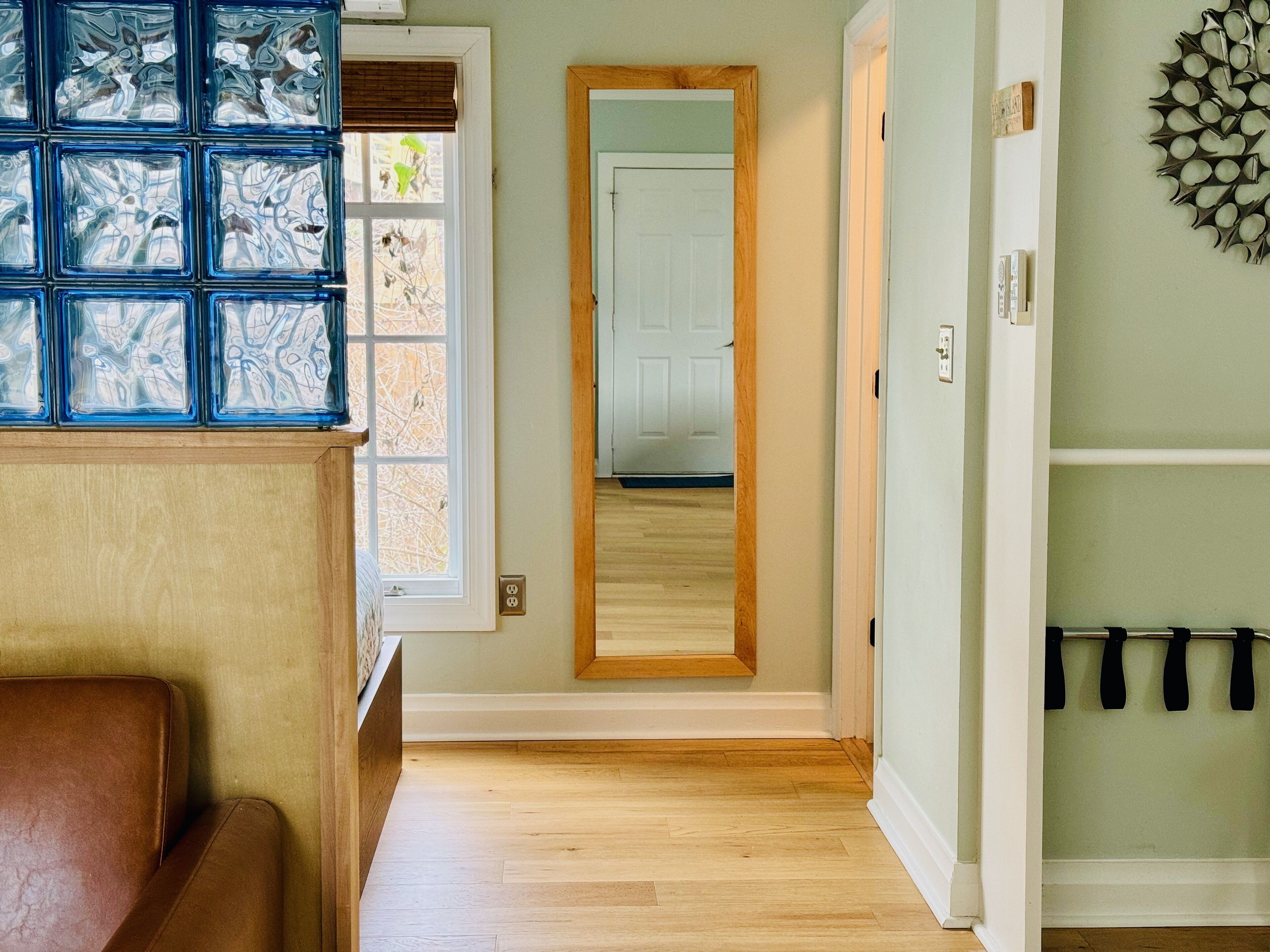 A hallway with a wooden floor, a brown leather chair, a glass block wall, and a door leading to another room.