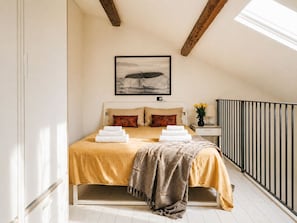 Ein Schlafzimmer mit Bett, Nachttisch, Lampe, einem Bild an der Wand und einem Fenster.