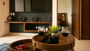 Un soggiorno moderno con un tavolino in legno su cui sono posizionati due bicchieri di vino rosso e una piccola pianta in vaso. Si vede anche un vassoio con fragole.