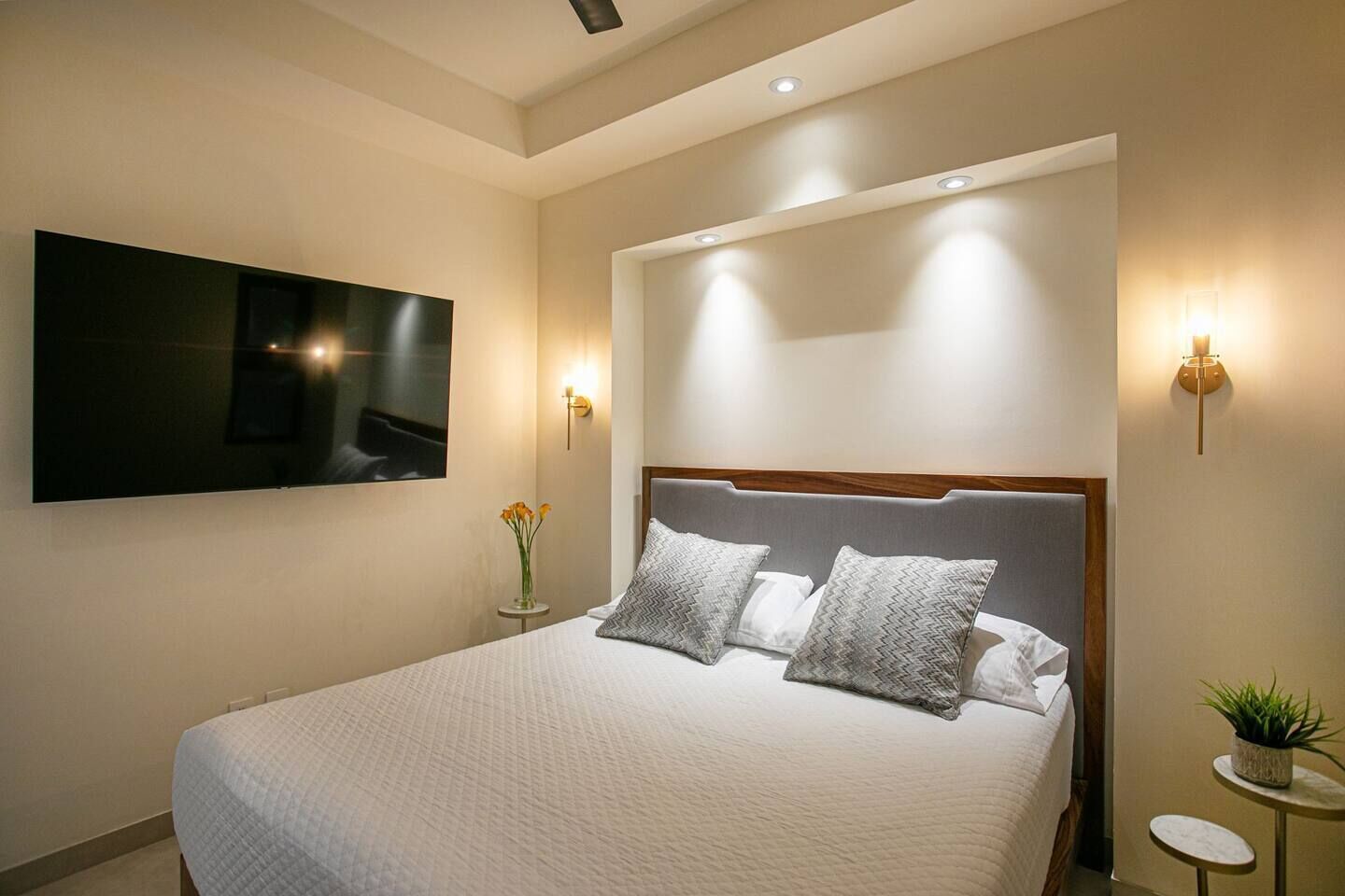 A modern hotel room with a large bed, a flat-screen TV mounted on the wall, and two bedside tables with lamps.