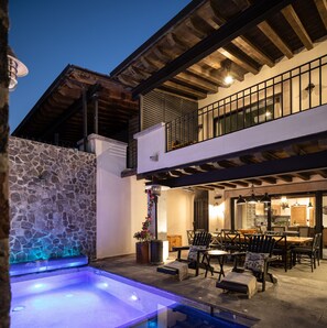 A modern outdoor pool area with stone walls, a wooden deck, and a dining area with outdoor furniture. - Private Pool, Elegant La Escondida 5BR (San Miguel de Allende)