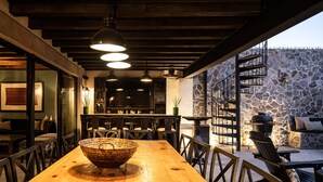 Una mesa de comedor de madera con sillas, una pared de piedra y una escalera que lleva a un espacio al aire libre.
