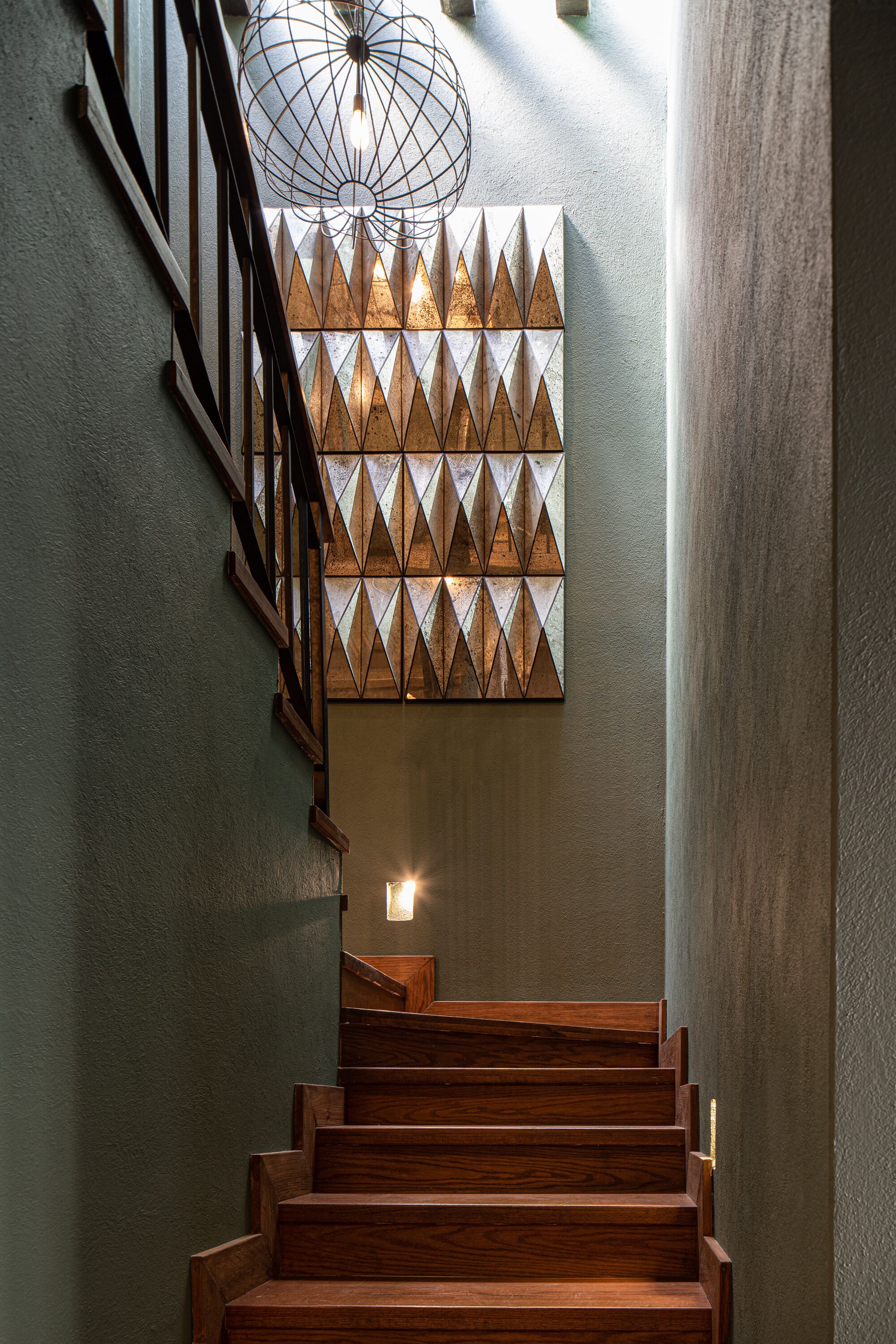 Un escalier en bois, avec une œuvre d’art géométrique accrochée au mur au-dessus.