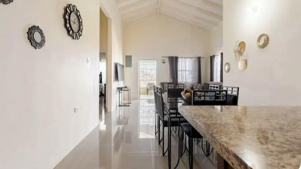 A spacious kitchen with a high ceiling, a dining area with a marble countertop, and decorative wall mirrors. - New Quiet Gated Ocean View Home (Trelawny)