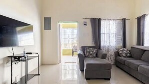 A living room with a sofa, ottoman, and a TV on a stand. - New Quiet Gated Ocean View Home (Trelawny)