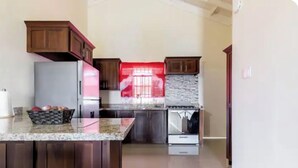 A kitchen with a granite countertop, stainless steel appliances, and wooden cabinets. - New Quiet Gated Ocean View Home (Trelawny)