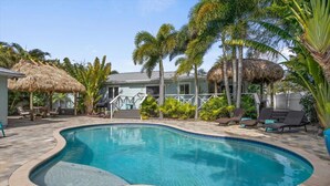 A swimming pool with a curved edge, surrounded by lounge chairs and palm trees.