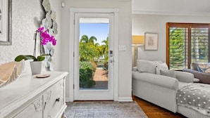 A room with a white dresser, a gray rug, a striped sofa, and a view of a garden through a glass door.