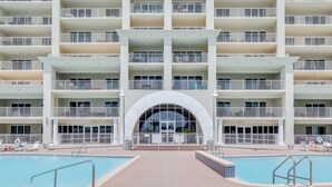 Een meerhoog hotel met een centrale, gebogen entree, twee zwembaden en balkons.