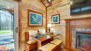 A cozy cabin interior with a wooden dining table, benches, a fireplace, and artwork on the walls.