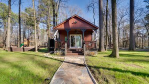A wooden cabin with a porch, surrounded by trees and a stone pathway leading to it.