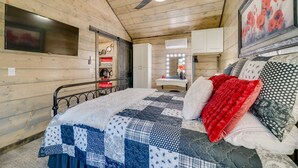 Een gezellige slaapkamer met een houten plafond, een bed met sprei, een plafondventilator en een spiegel met verlichting.