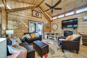 Een gezellig chaletinterieur met een open haard, houten wanden, een plafondventilator en een eethoek.
