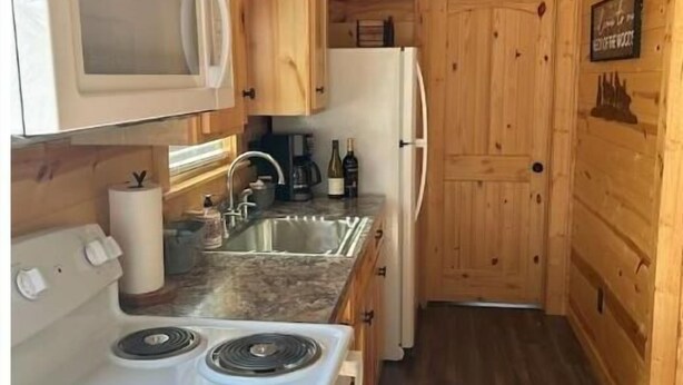 Een kleine keuken met houten kastjes, een magnetron, een fornuis en een koelkast.