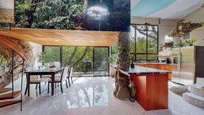 A modern kitchen with a stone island, large windows, and a dining area with a glass table and chairs. - Artsy Riverfront Jungle Retreat: River Pool & Hot Tub in living room (Rivas)