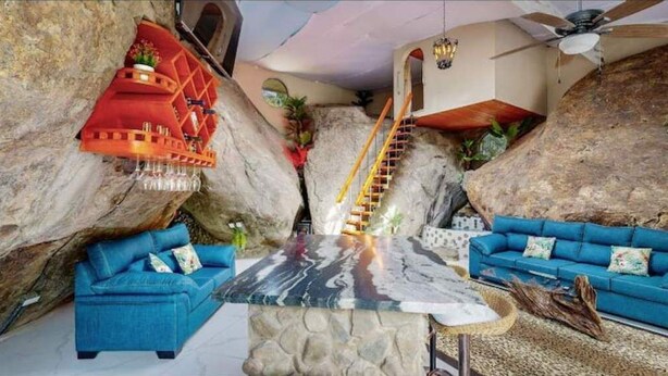 A room with a central marble table, two blue sofas, a red decorative piece, and a staircase leading to a higher level. - Artsy Riverfront Jungle Retreat: River Pool & Hot Tub in living room (Rivas)