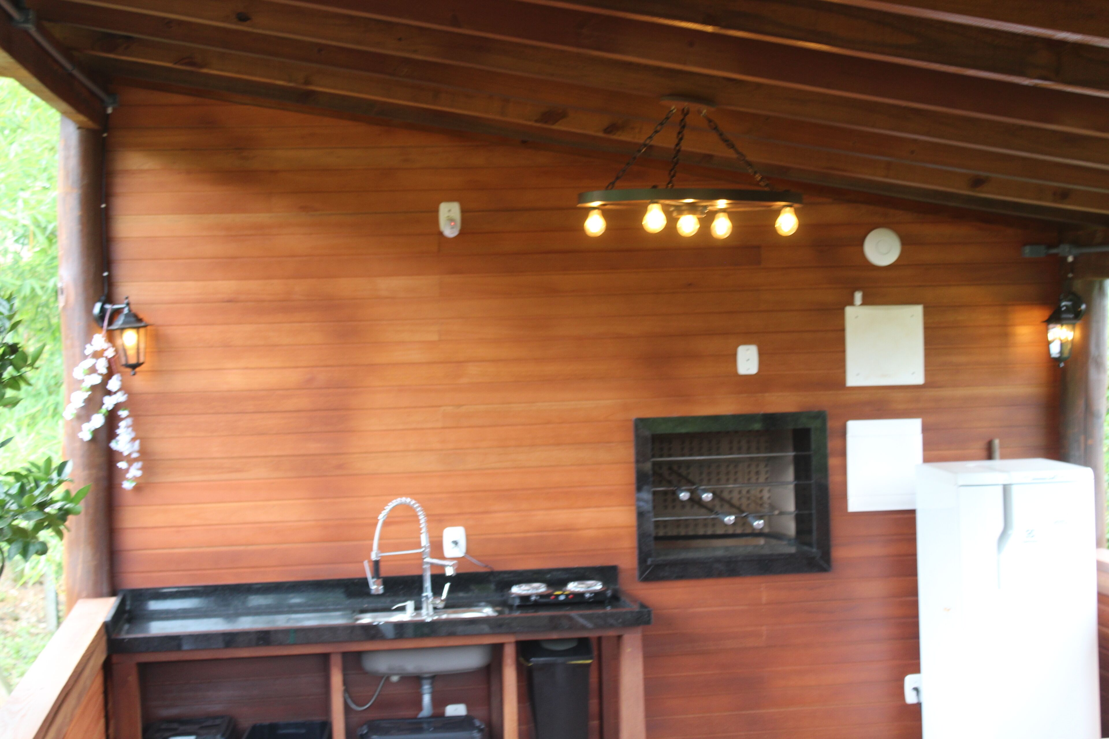 Una cabaña de madera con zona de cocina que incluye un lavamanos, encimera e iluminación colgante.