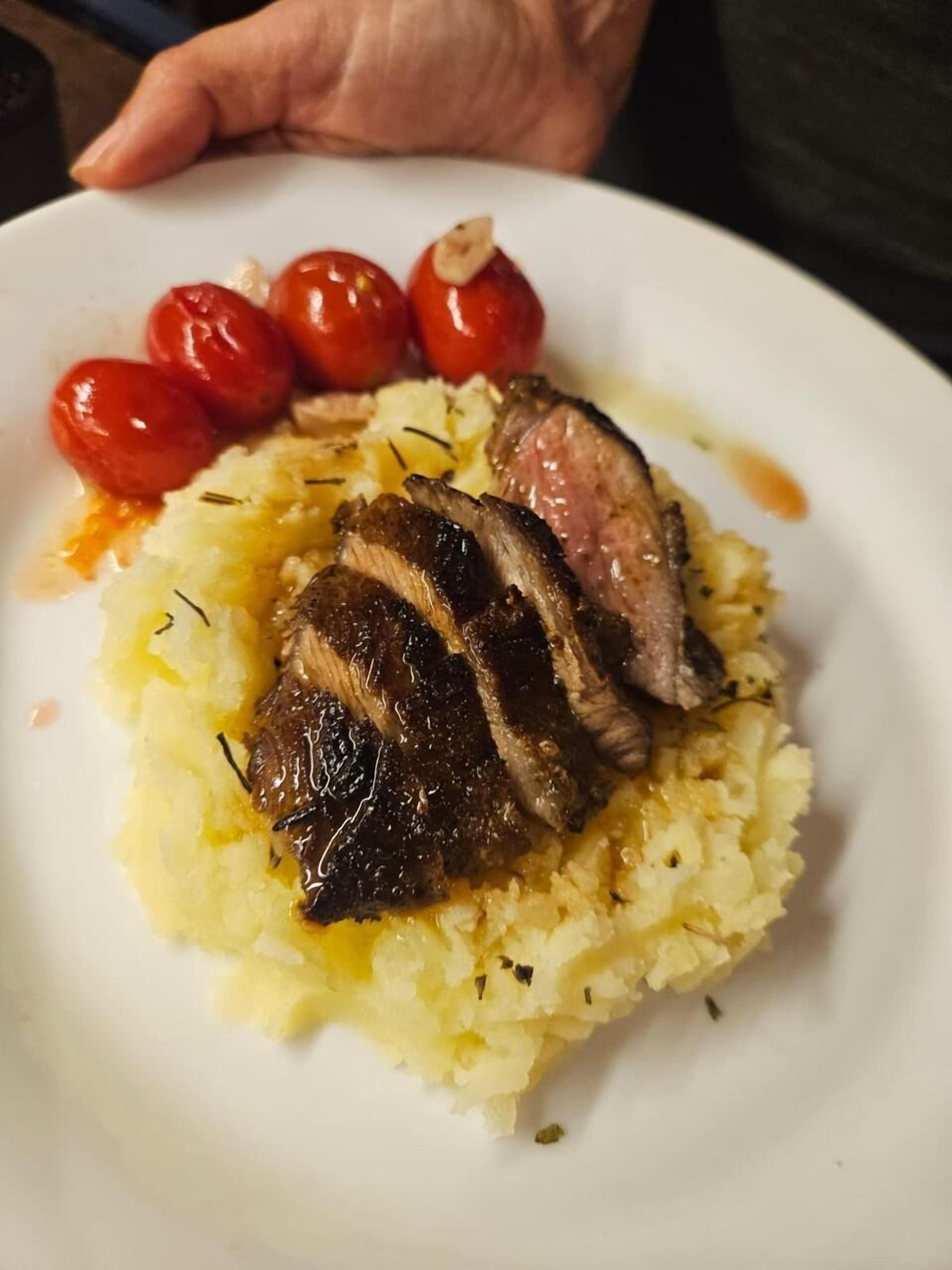 Un plato con carne en rodajas, puré de papas y tomates cherry.