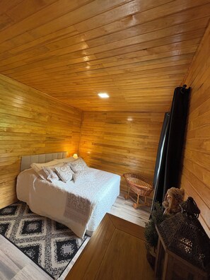 A cozy wooden room with a bed, a small table, and a hanging chair.