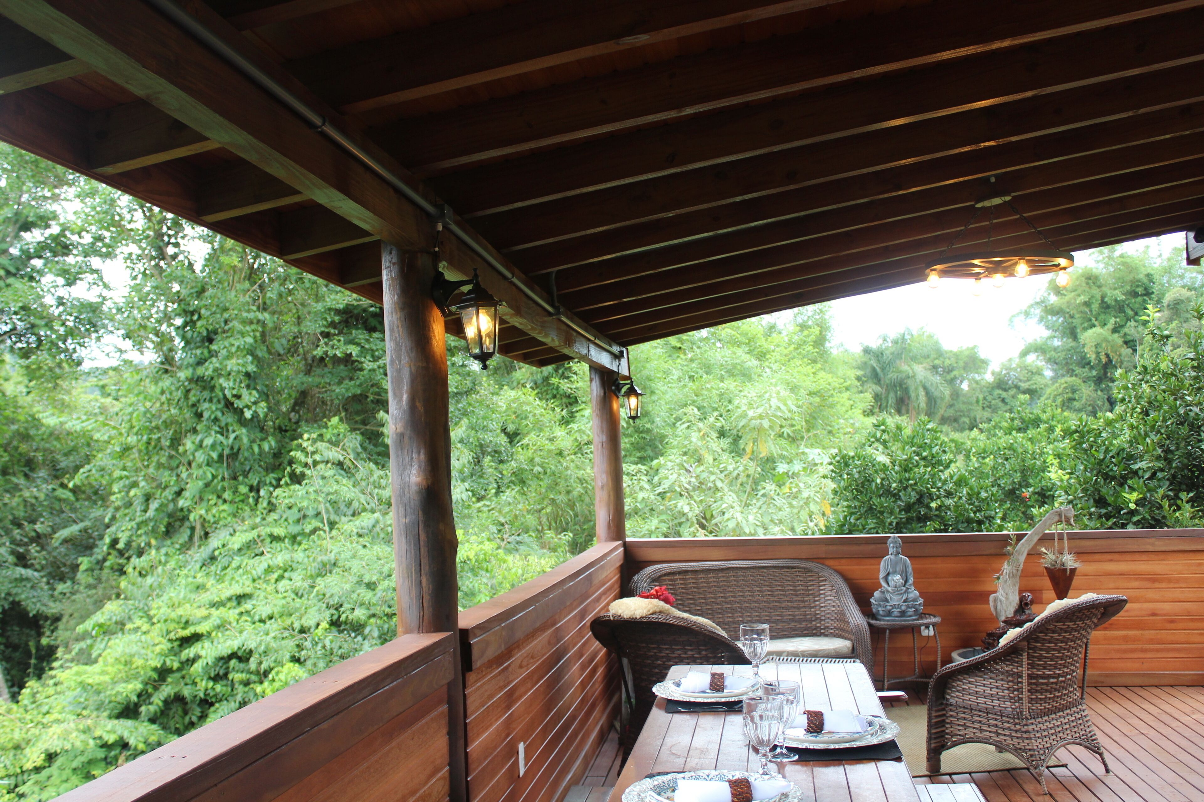 Una terraza exterior de madera con mobiliario de mimbre, una estatua de Buda y una planta en maceta.