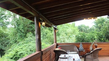 Una terraza exterior de madera con mobiliario de mimbre, una estatua de Buda y una planta en maceta.