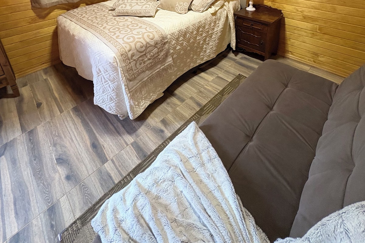 Ein Zimmer mit Holzwänden, einem Bett, einem Nachttisch, einer Lampe und einem Sofa.