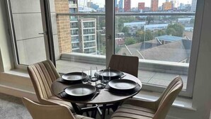 Un coin repas avec une table ronde et quatre chaises, de grandes fenêtres offrant une vue sur la ville et une porte-fenêtre coulissante.