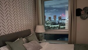 Une chambre d’hôtel avec un grand lit, une vue sur le paysage urbain illuminé la nuit et un mur orné d’un motif en chevrons.