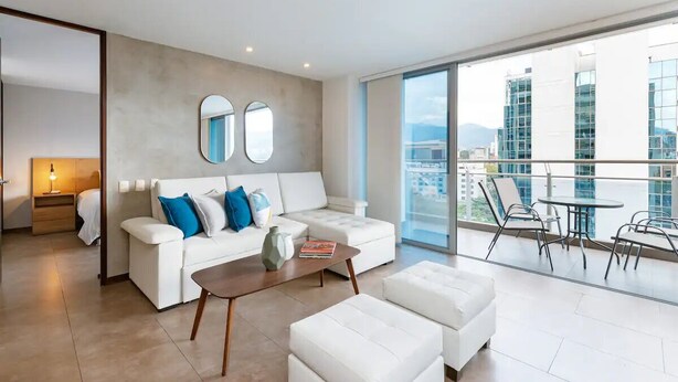 Una sala de estar moderna con un sofá blanco, una mesa de centro y un balcón con mobiliario exterior.