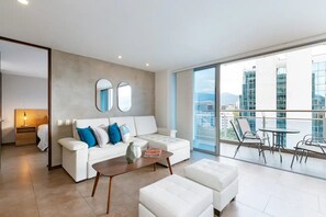 Un salon moderne avec un canapé blanc, une table basse et un balcon aménagé avec du mobilier d’extérieur.