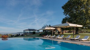 Ein Schwimmbad mit Liegestühlen und Sonnenschirmen, ein Wintergarten und ein Steinhaus mit Garten.