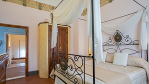 A four-poster canopy bed with a decorative headboard, a wooden wardrobe, and a mirror on the wall.