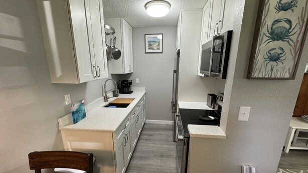 Cocina compacta con armarios blancos, microondas integrado y cafetera.