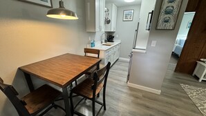 Un comedor con una mesa y sillas de madera, una lámpara colgante y una cocina al fondo.