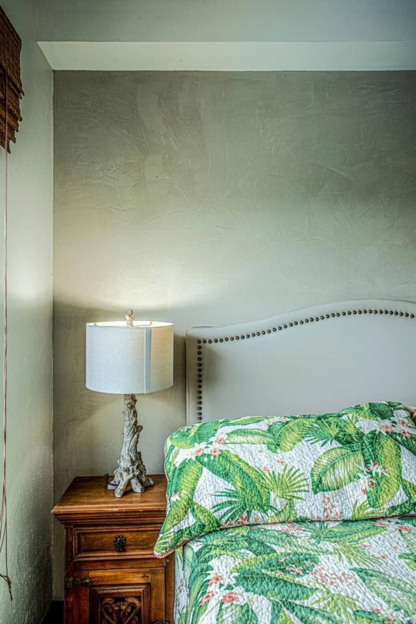 Un dormitorio con cama, mesita de noche con lámpara y pared con textura.