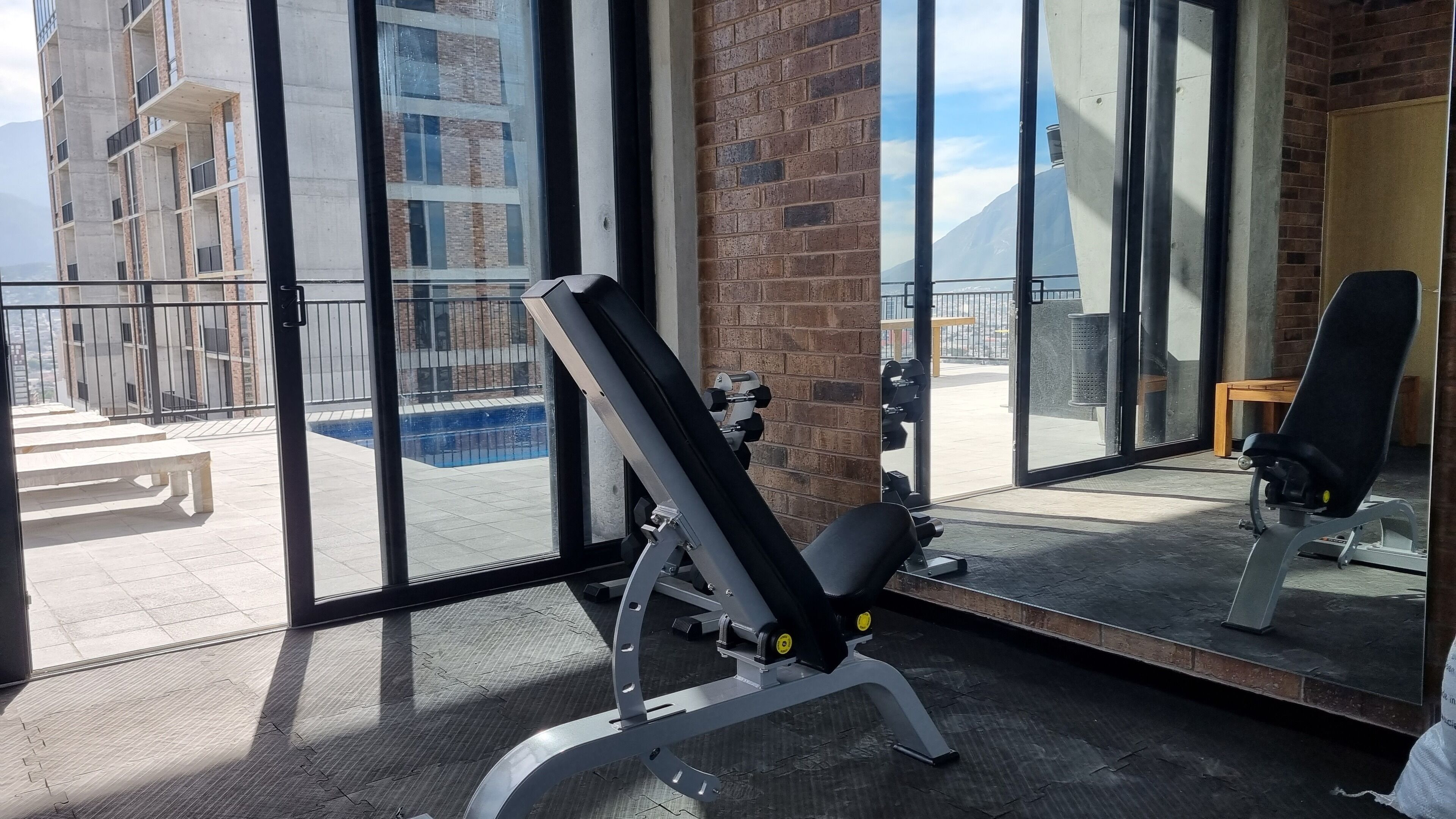 A gym with exercise equipment, a pool, and a view of a building with a brick facade.