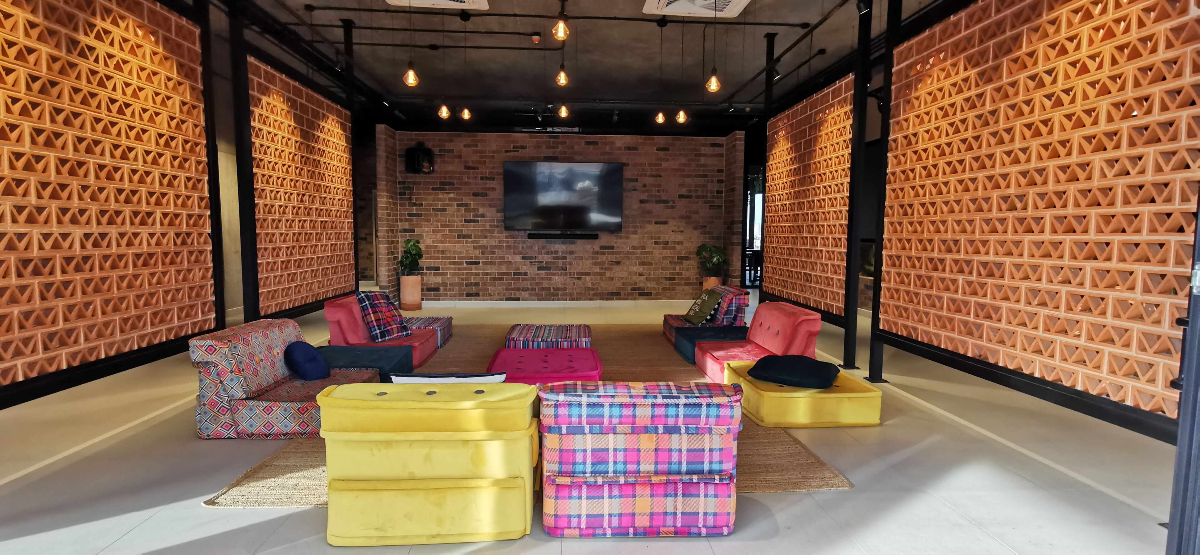 A modern lounge area with brick walls, a flat-screen TV, and colorful seating arrangements.