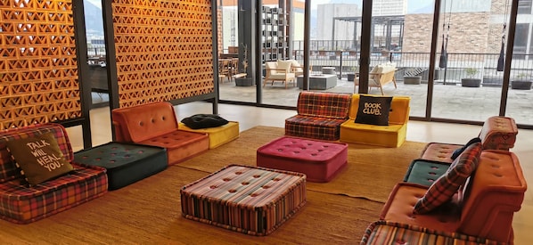 Un área de lounge moderna con asientos de colores y diseños, y vistas del paisaje urbano a través de amplias ventanas.