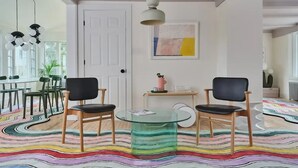 A modern living room with two black chairs, a glass coffee table, and a colorful rug.