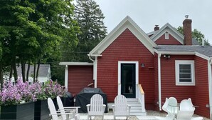 A red house with a covered grill, white outdoor furniture, and a dog on the porch.