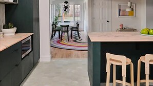 A modern kitchen with dark cabinetry, a central island with stools, and a dining area with a colorful rug.