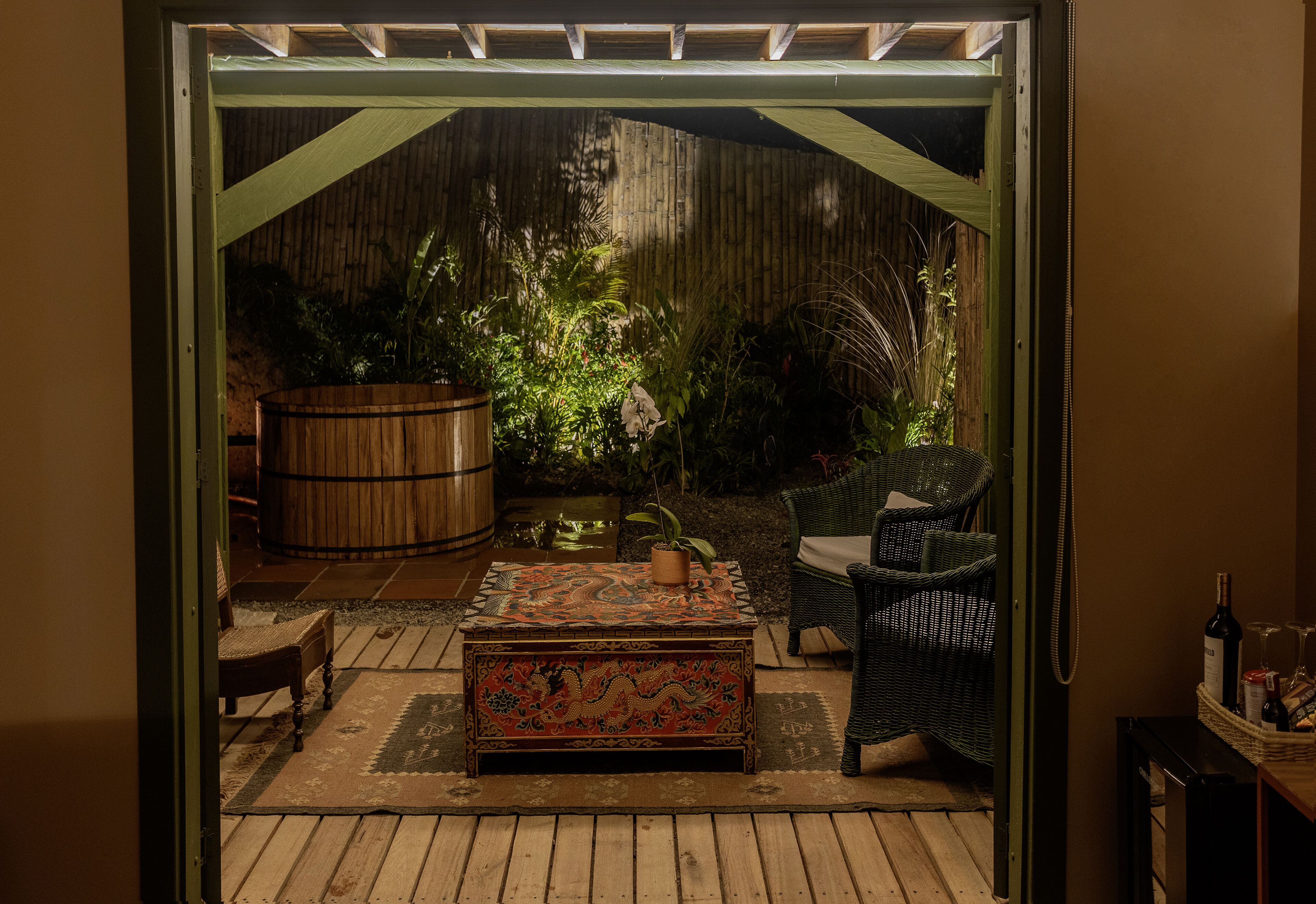 Un patio abierto con un banco de madera, un cofre decorativo, muebles de mimbre y un barril grande.