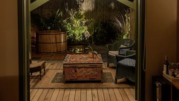 Un patio abierto con un banco de madera, un cofre decorativo, muebles de mimbre y un barril grande.