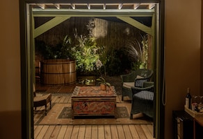 Un patio abierto con un banco de madera, un cofre decorativo, muebles de mimbre y un barril grande.