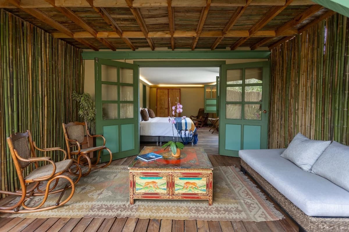 A room with a bed, a sofa, a rocking chair, and a coffee table with a book and an orchid.