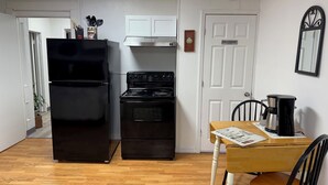 Une cuisine de taille réduite avec un réfrigérateur noir, une cuisinière et une machine à café posés sur une table en bois.