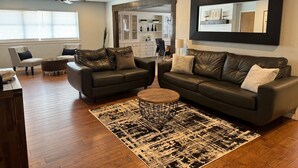 Ein modernes Wohnzimmer mit zwei dunklen Ledersofas, einem Couchtisch und einem gemusterten Teppich.