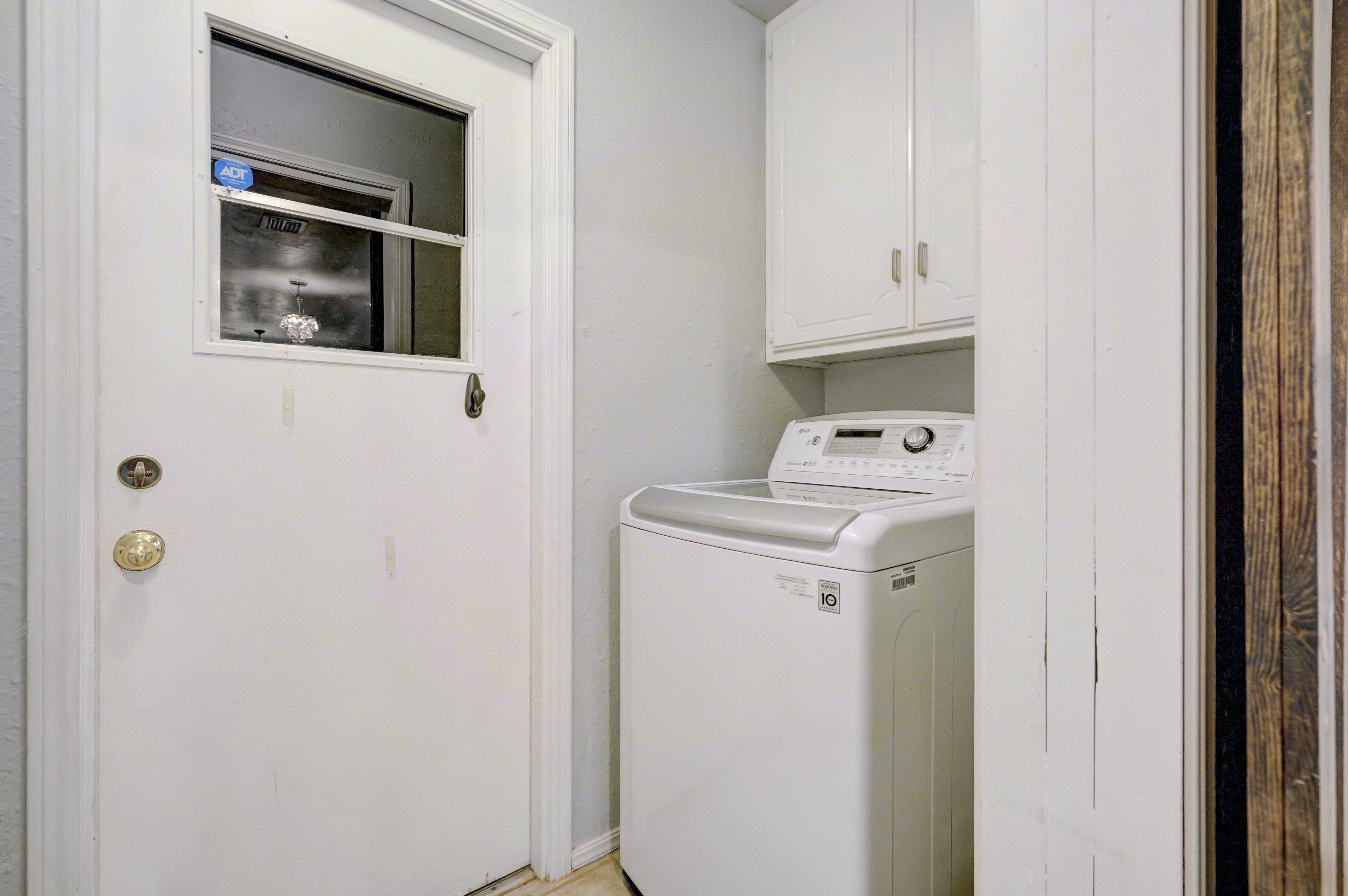 Une buanderie équipée d’un lave-linge et d’un sèche-linge à chargement frontal, d’une porte avec une fenêtre et d’un meuble blanc placé au-dessus du sèche-linge.