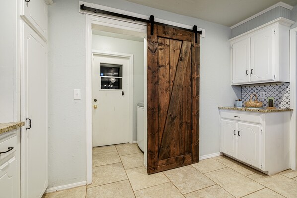 A kitchen with white cabinets, a wooden barn-style door, and a tiled backsplash.